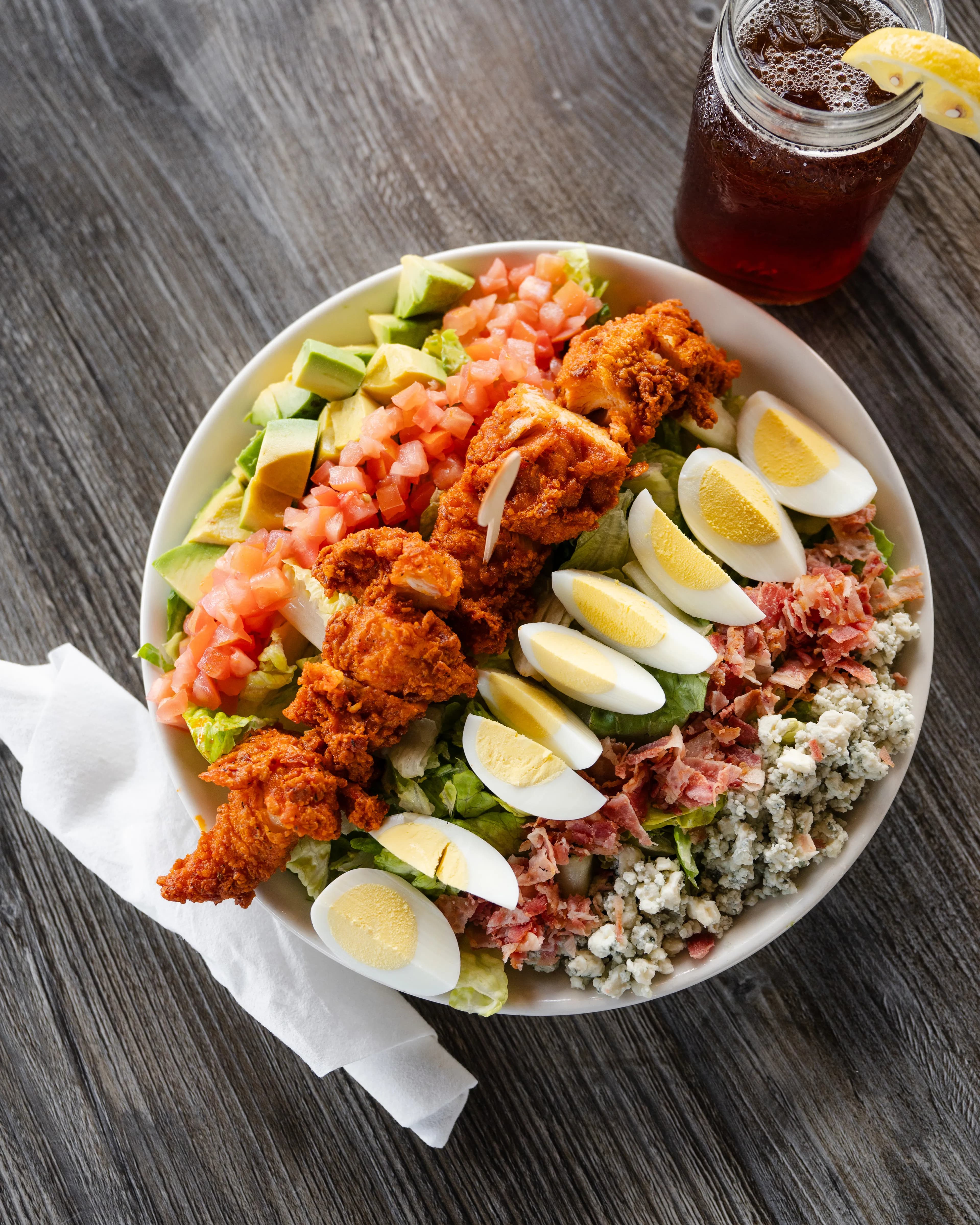A vibrant cobb salad featuring crispy fried chicken, hard-boiled eggs, bacon, blue cheese, avocado, and diced tomatoes