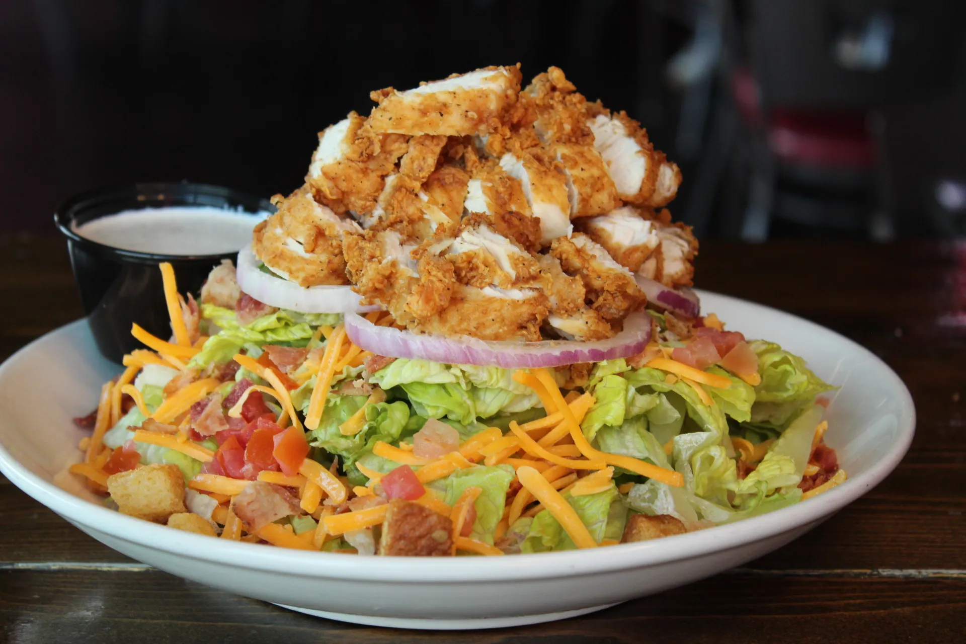 A hearty salad topped with crispy fried chicken, fresh vegetables, and a side of dressing.