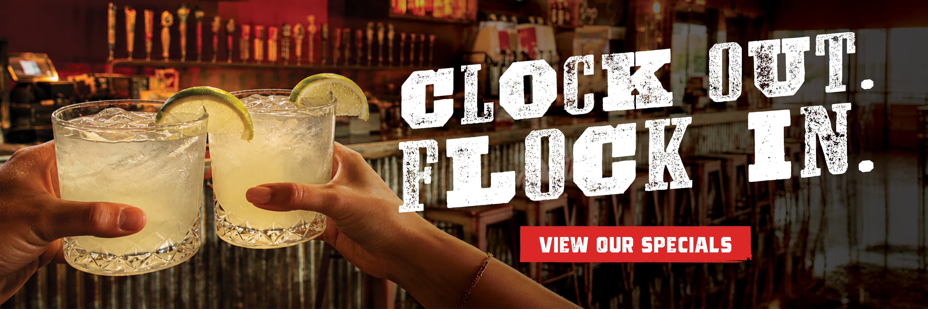Two hands holding glasses of refreshing drinks with lime slices, set against a bar backdrop.