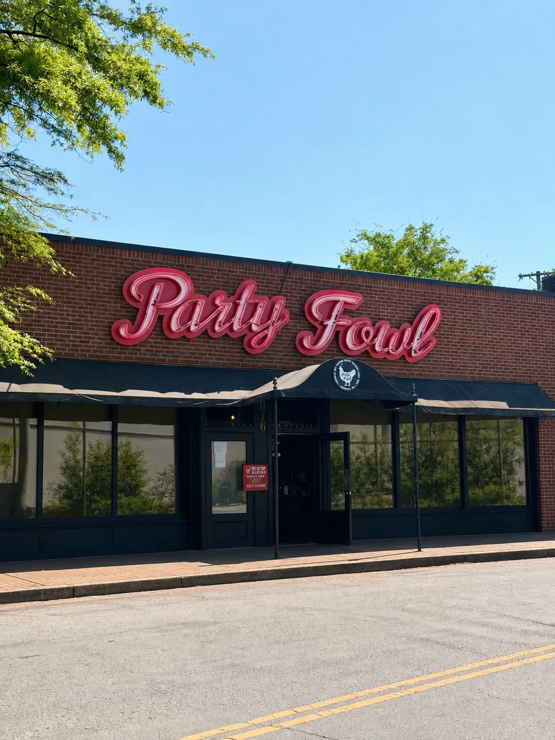 A brick storefront with a large neon sign reading 'Party Fowl' under a clear blue sky.