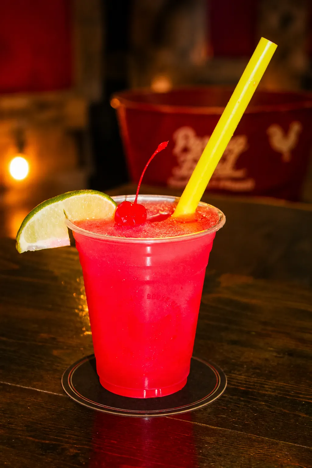 Cherry Limeade A vibrant cherry limeade garnished with a cherry and lime slice, served in a plastic cup with a yellow straw.
