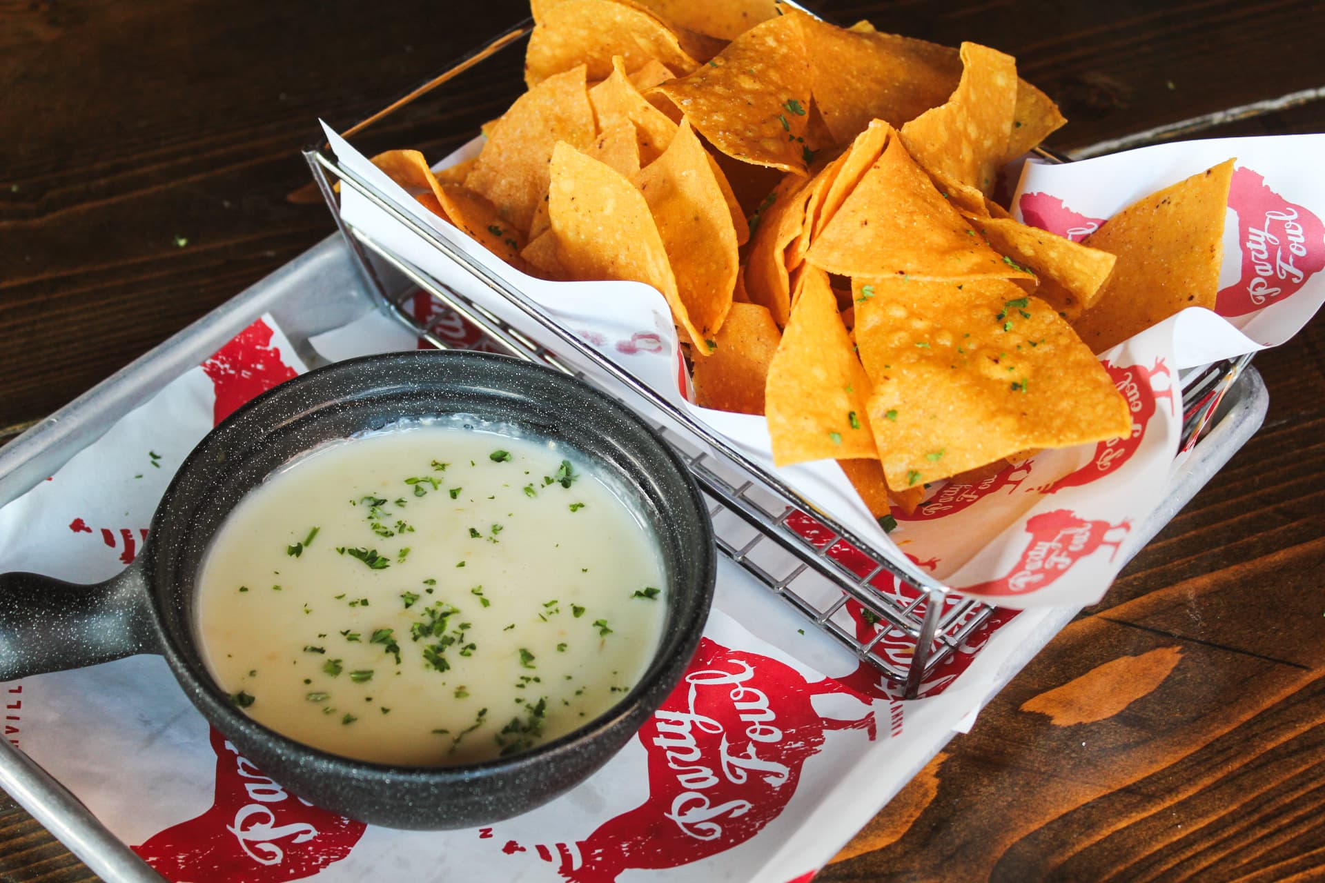 Chips & Queso A plate of crispy tortilla chips served with a bowl of creamy queso dip, garnished with fresh herbs.