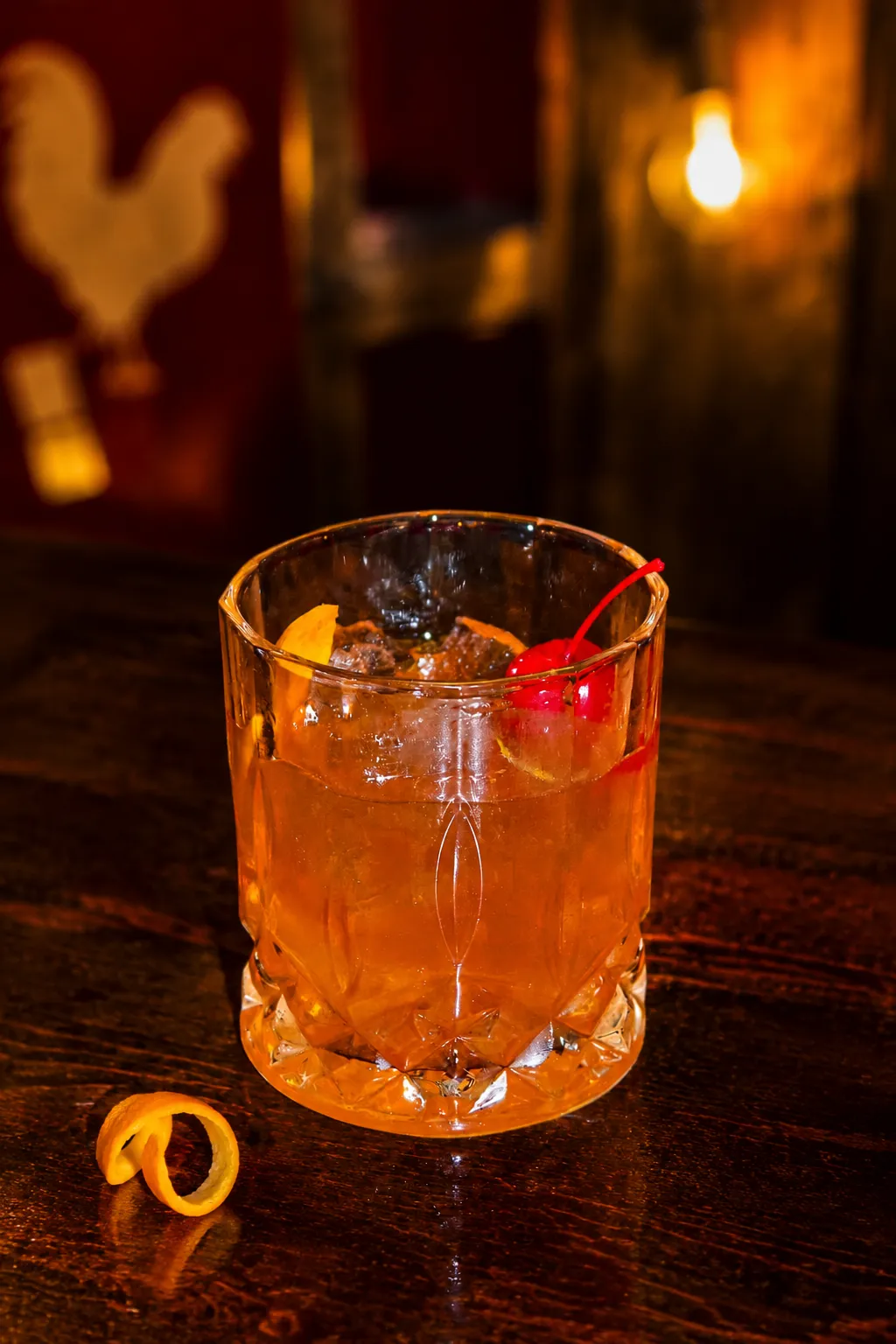Old Fashioned A classic Old Fashioned cocktail garnished with a cherry and orange peel, served in a dimly lit bar setting.