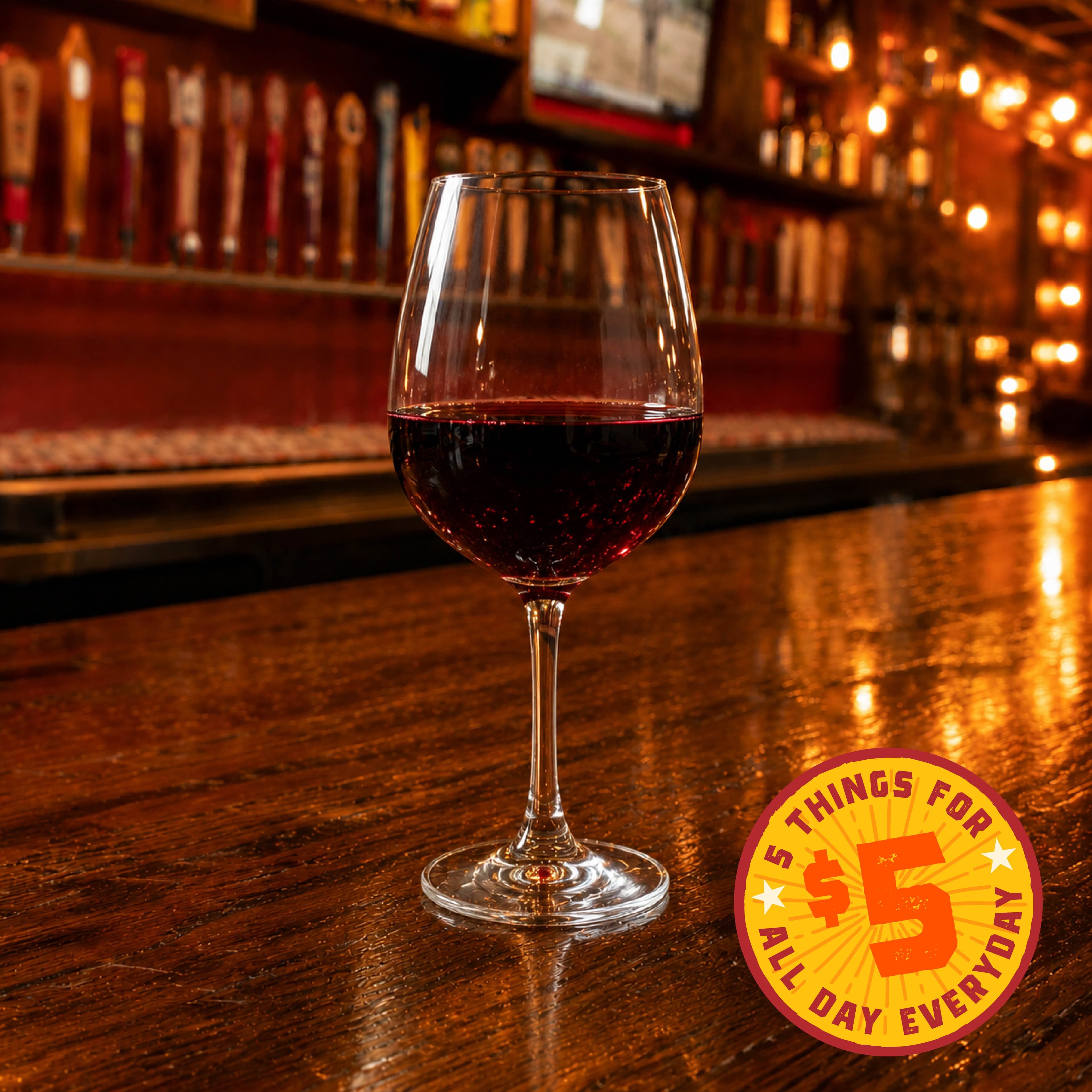 Happy Hour Image 02 A glass of red wine on a bar counter with a promotional sign in the foreground.