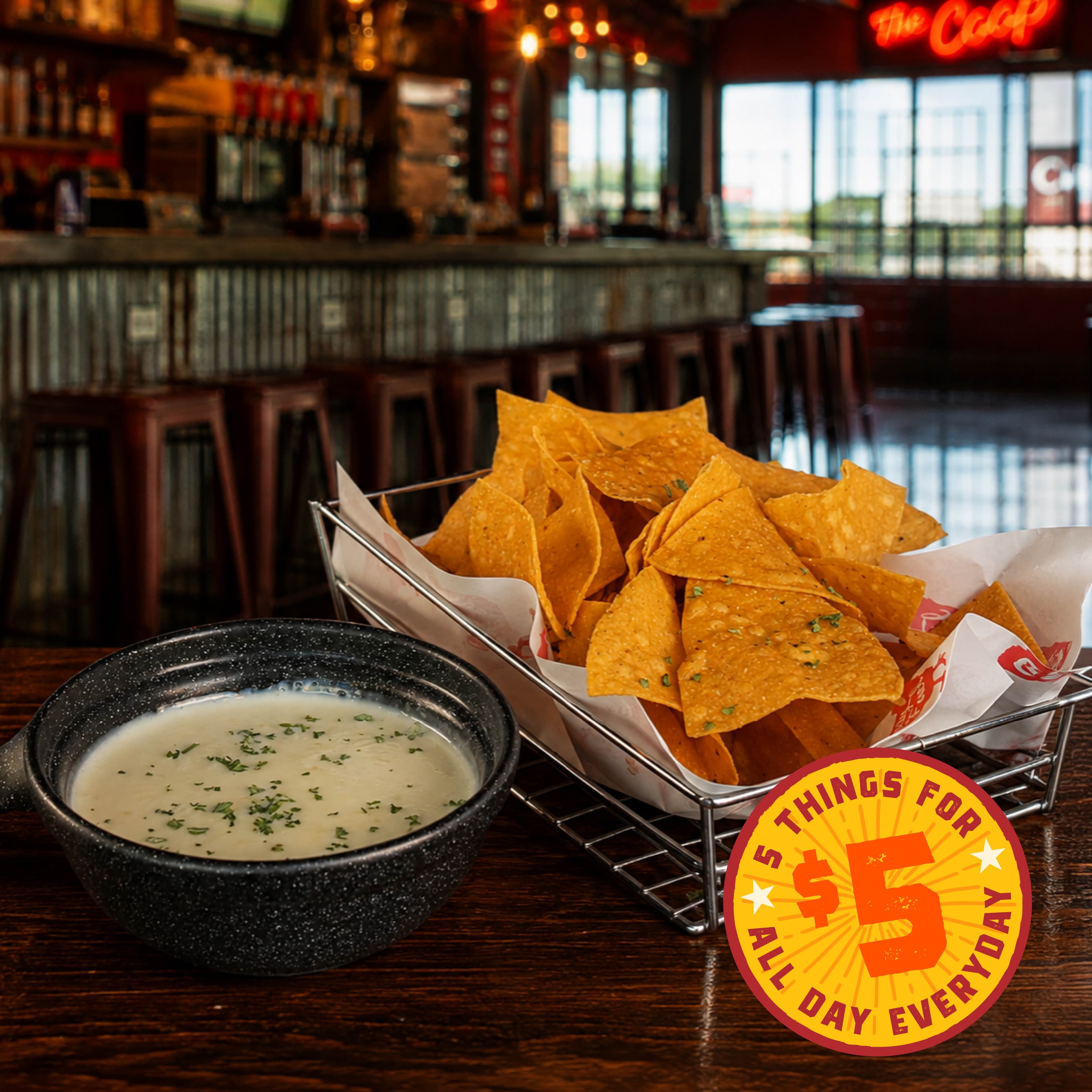 PF HappyHour Image 05 Nachos and queso dip in a bar setting with a promotional sign for $5 deals.