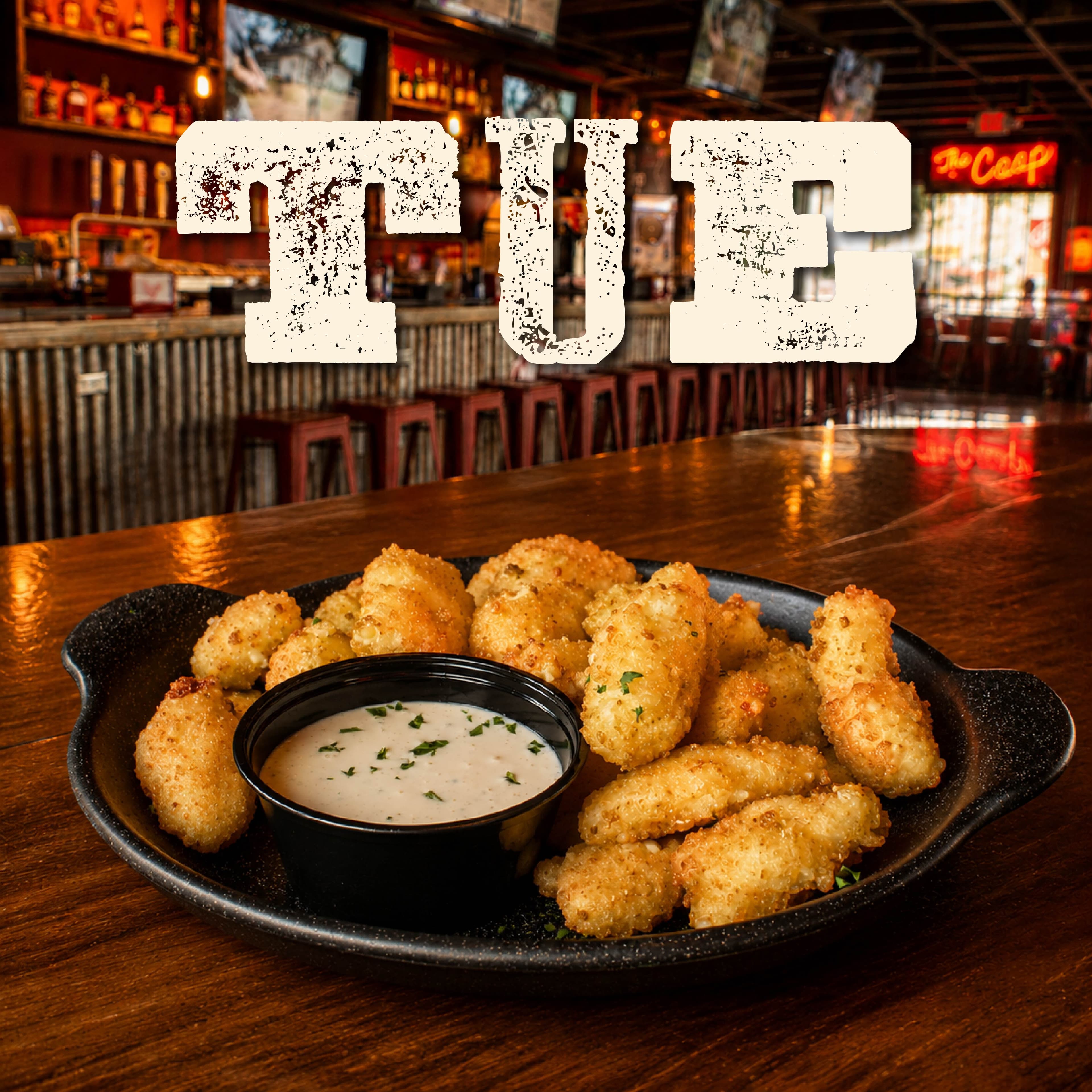 PF WeeklySpecials Image 02 Golden crispy fried cauliflower florets served with a creamy dipping sauce on a black plate in a cozy bar setting.