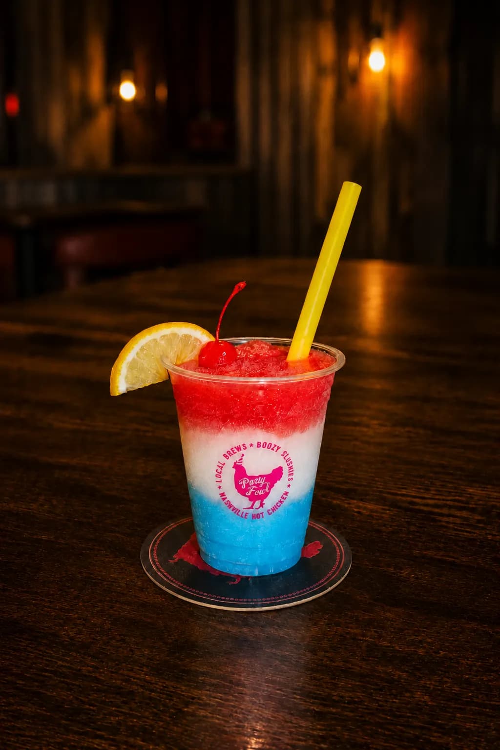 Willie Pop A vibrant red, white, and blue slushy drink garnished with a cherry and lemon slice, served in a branded cup