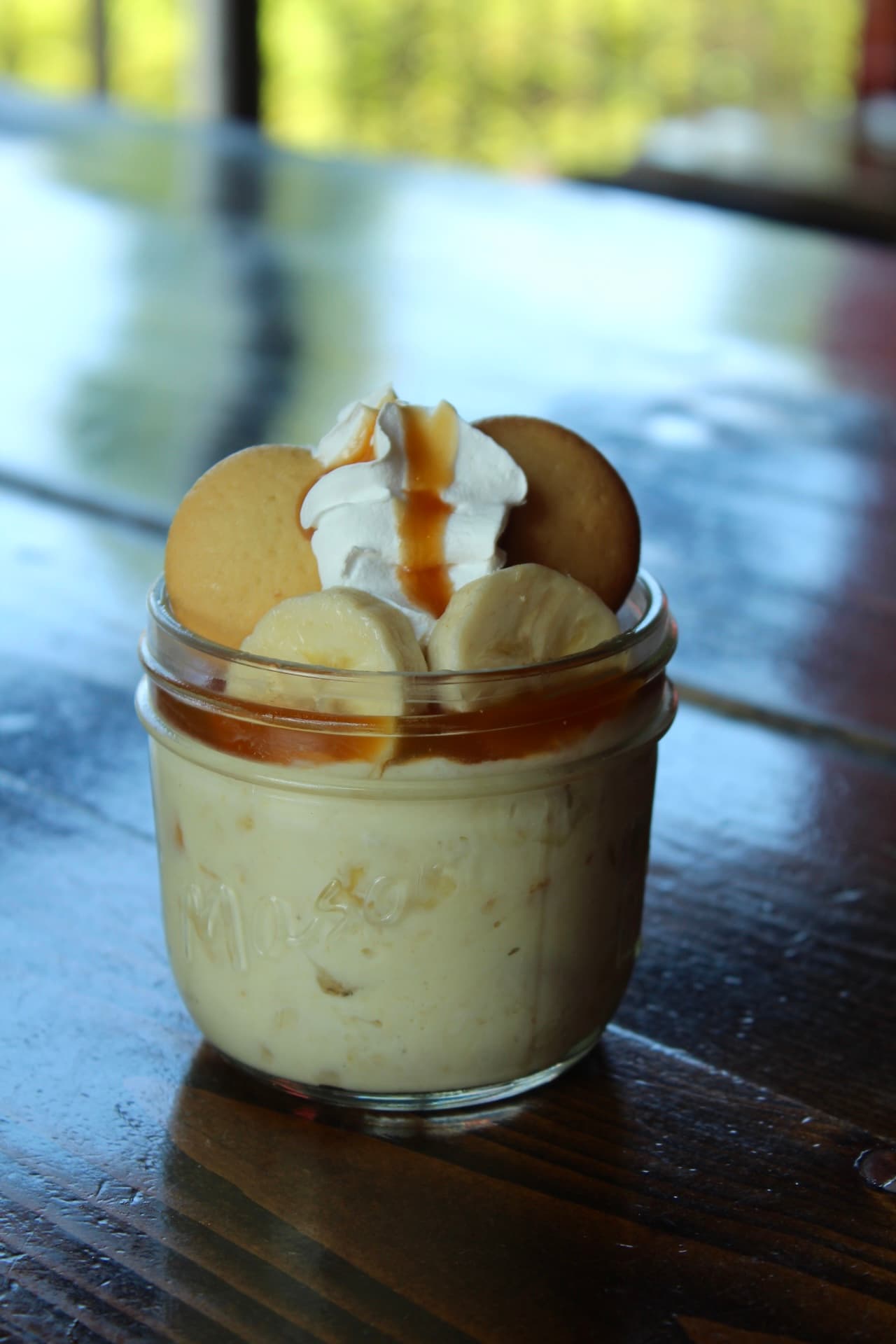 Bananapudding A jar of banana pudding topped with whipped cream, bananas, and cookies.