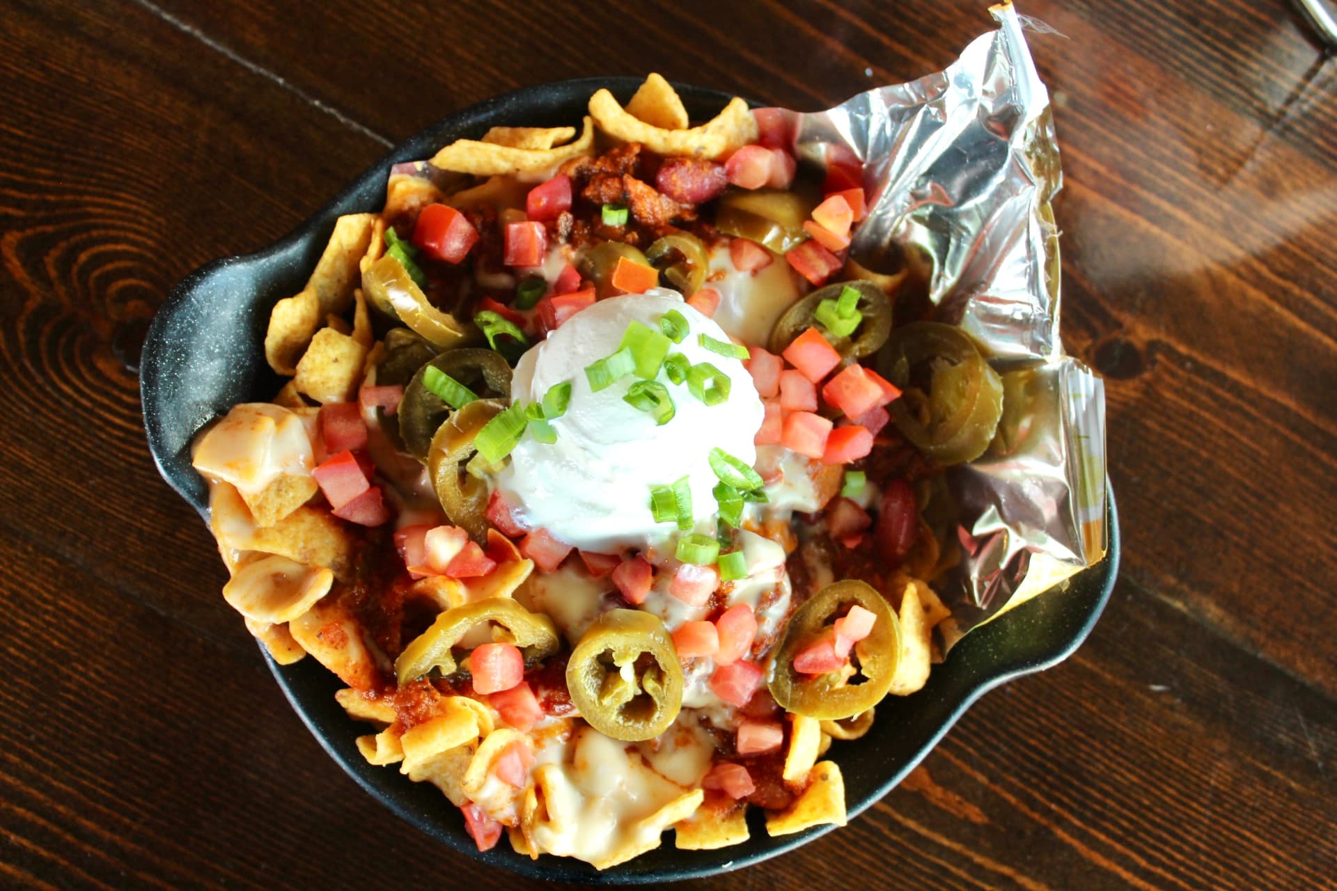 Brisket Frito Pie A hearty frito pie topped with brisket, jalapeños, diced tomatoes, and sour cream, served in a cast iron skillet.