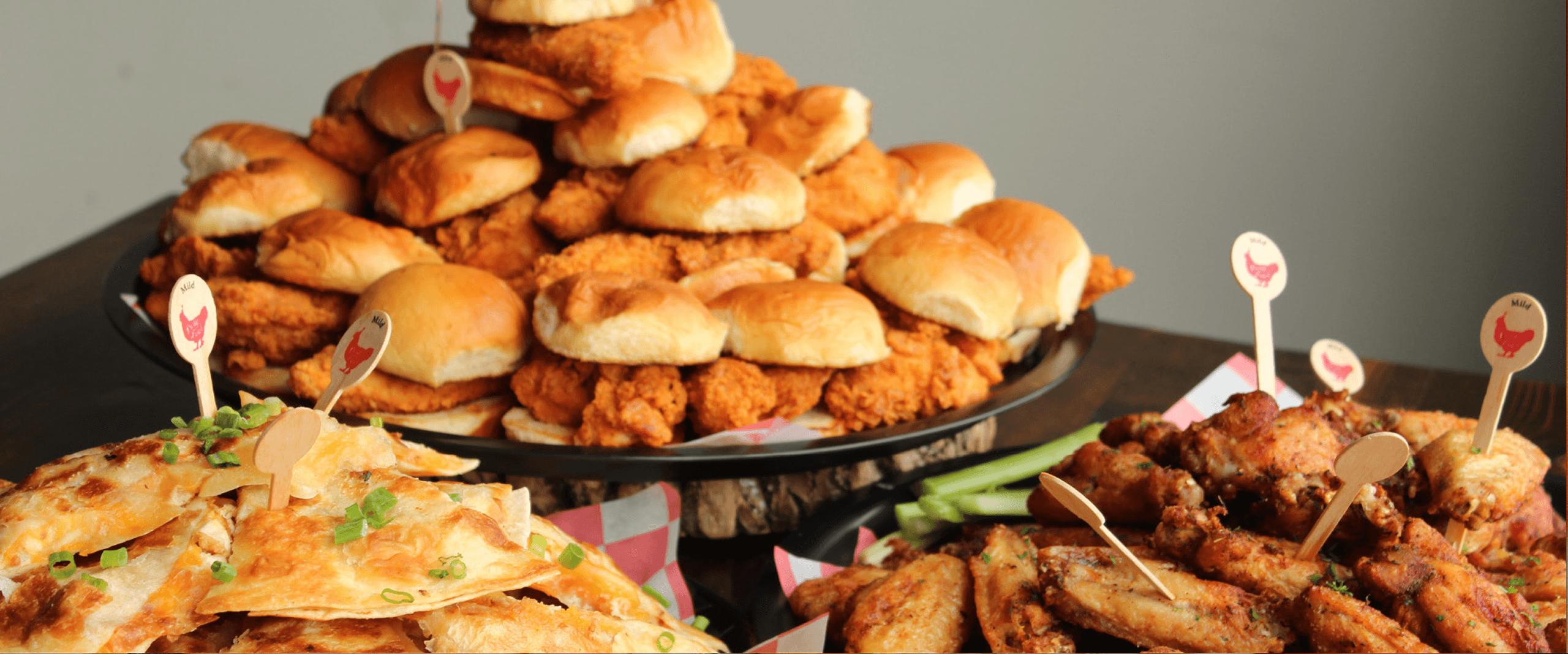 Catering Banner A tiered display of appetizers, including fried chicken sliders, nachos, and wings, perfect for a party or event.