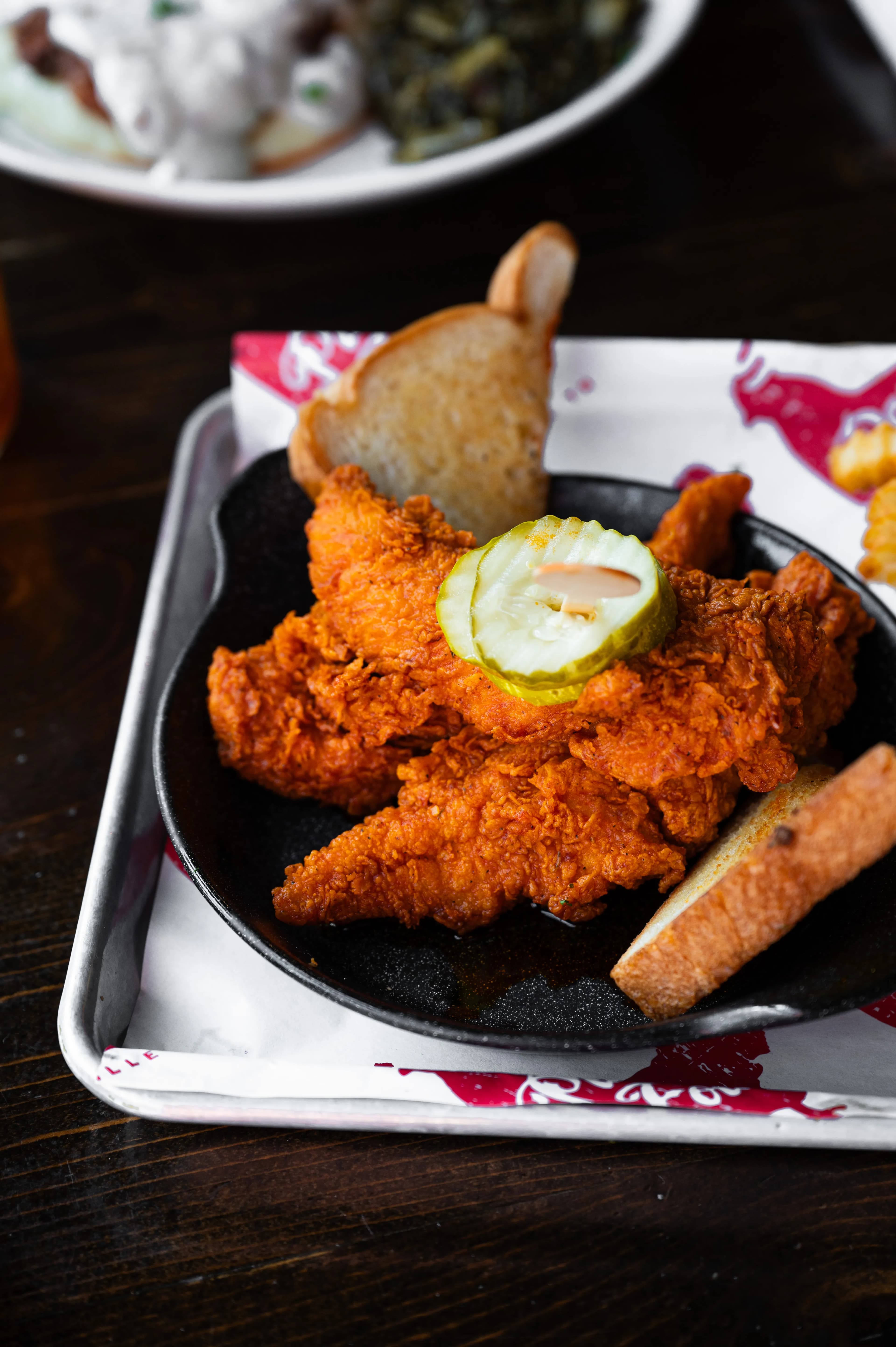 Chicken Tenders Golden crispy chicken tenders served with pickles and breadsticks on a black plate.