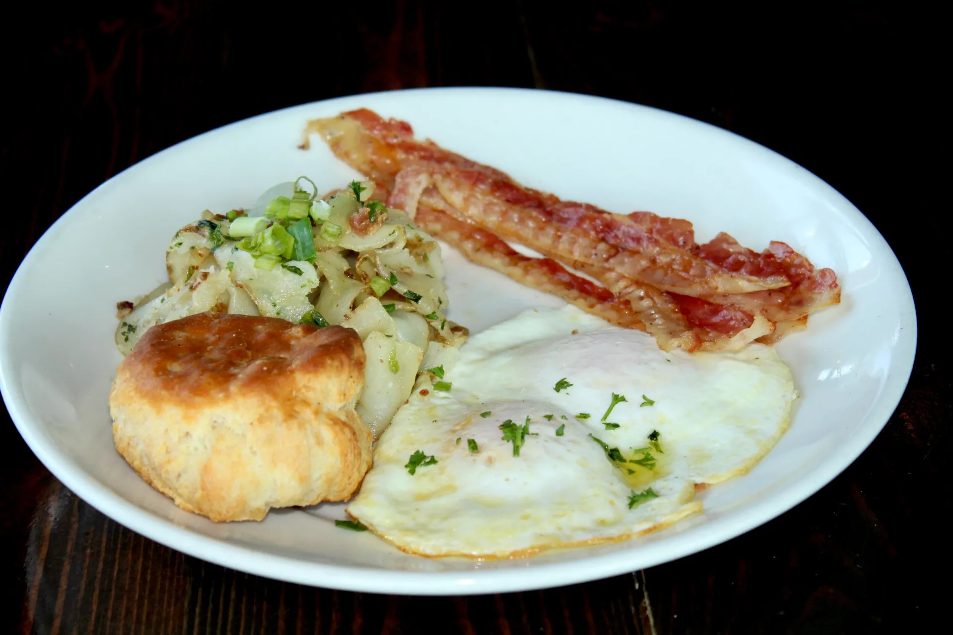 Coopsclassic A hearty breakfast featuring two sunny-side-up eggs, crispy bacon, a fluffy biscuit, and a side of sautéed onions garnished