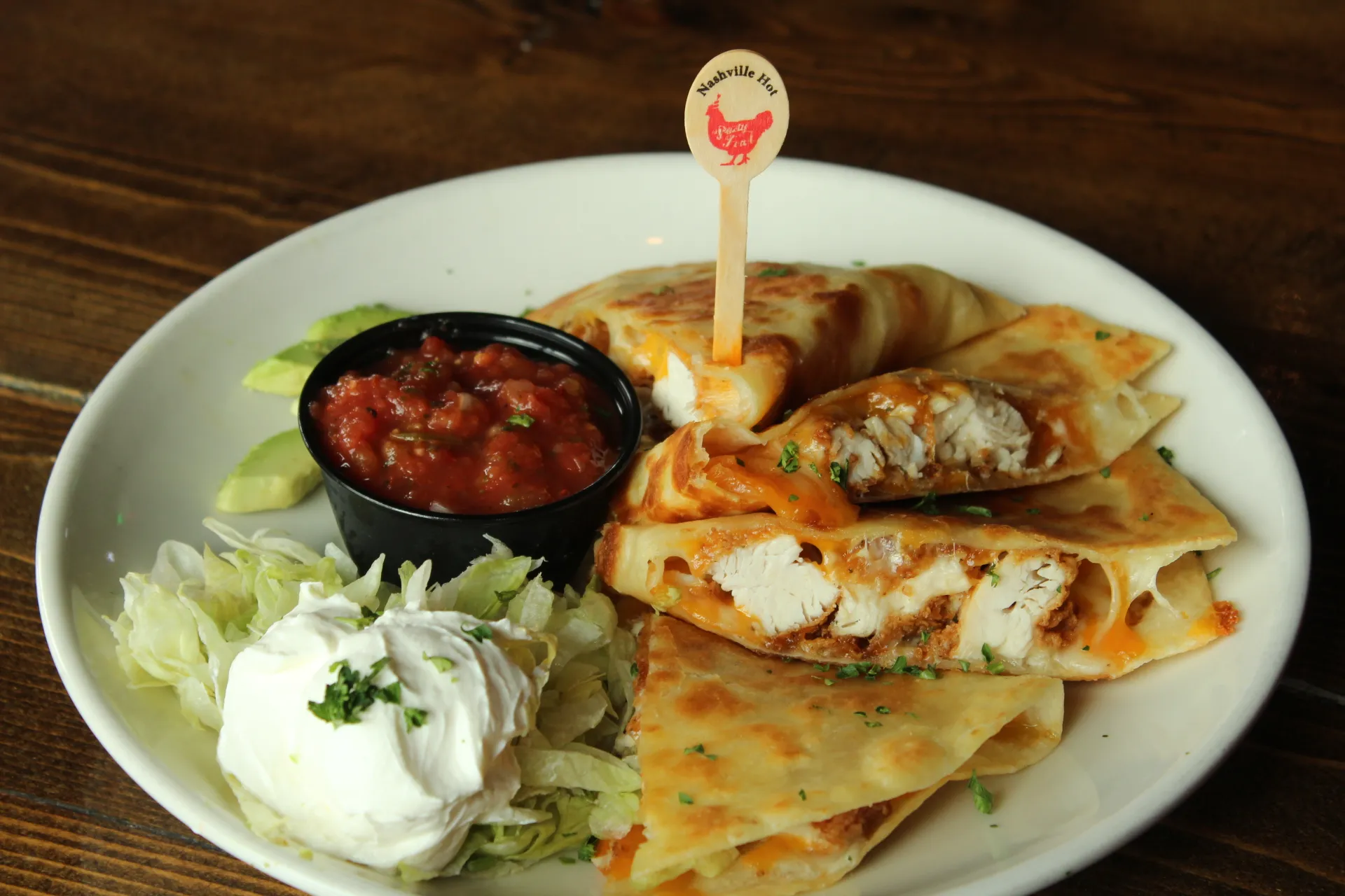 quesadillaa A plate of crispy chicken quesadillas with salsa, sour cream, and shredded lettuce.