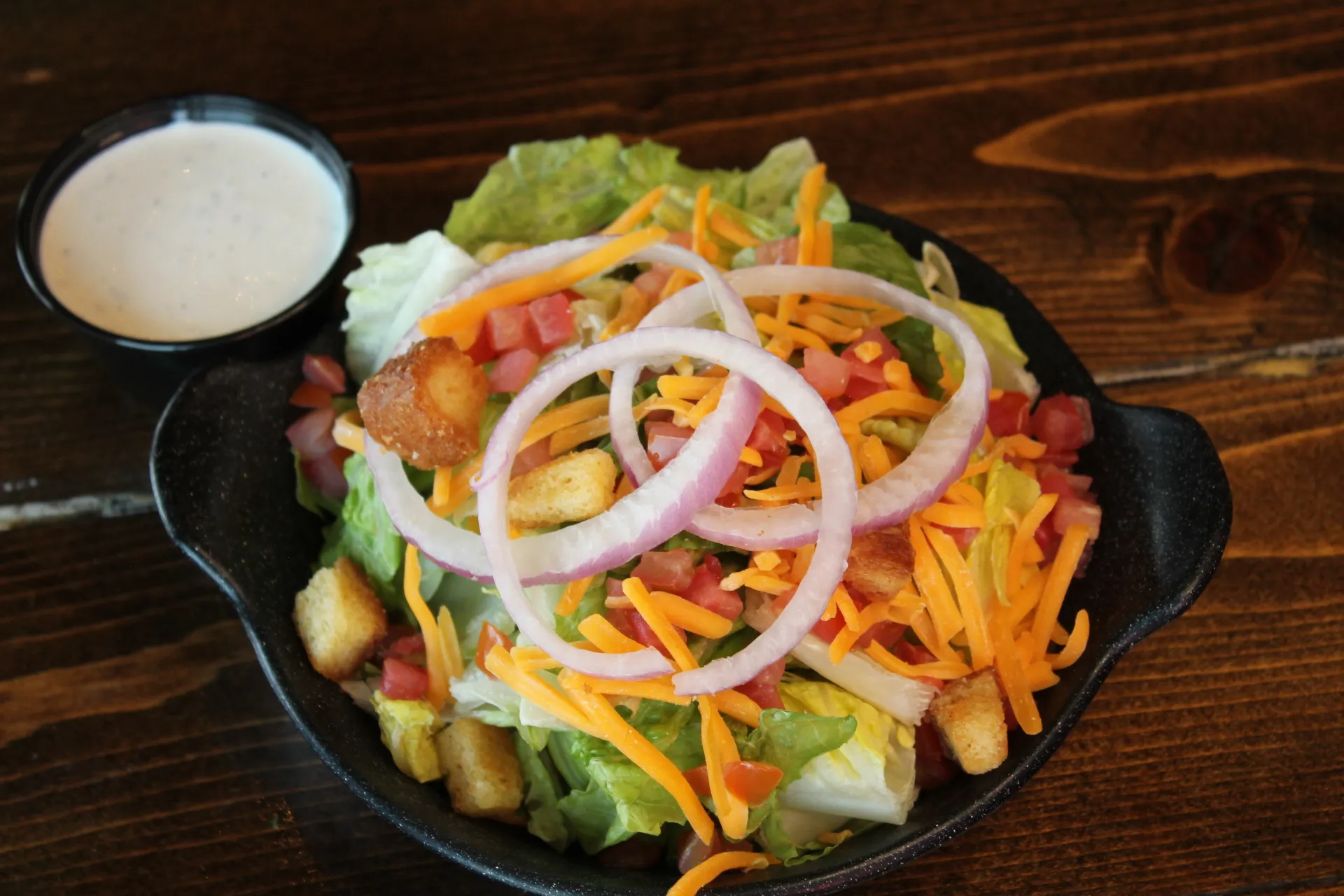 Side Salad A vibrant side salad with lettuce, tomatoes, shredded cheese, croutons, and red onion rings served with a creamy dressing.