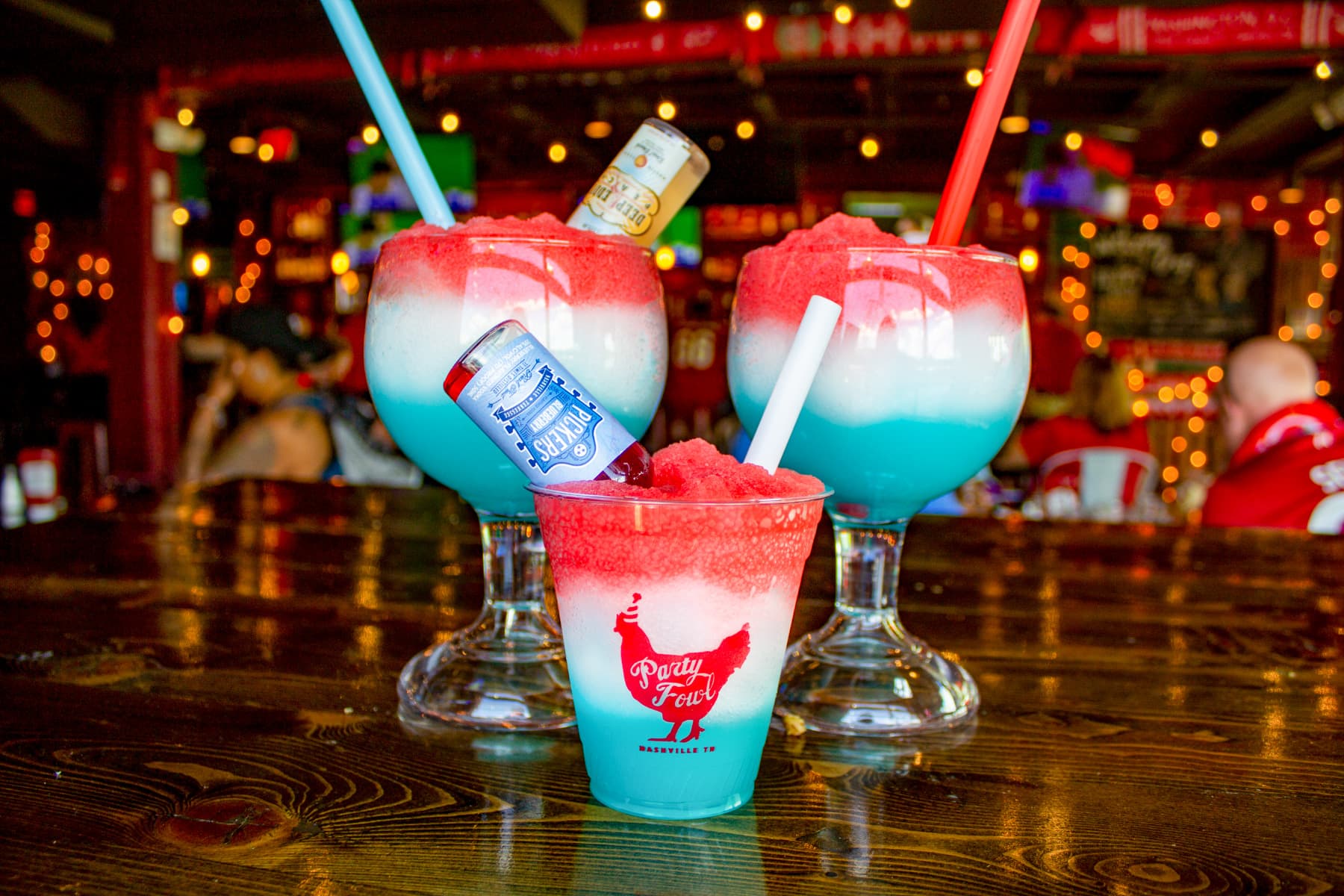 Willie Pops Boozy Slushies Colorful boozy slushies with layered red, white, and blue toppings in a festive bar setting.
