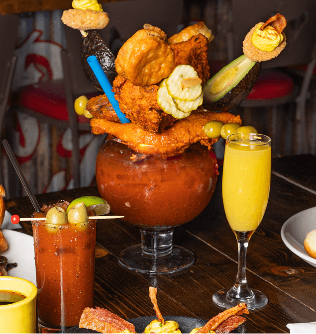 Zero Chilled Bloody Mary A vibrant Bloody Mary garnished with fried chicken, pickles, olives, and a lime, served with a mimosa on the side.
